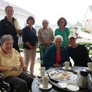 A group of women enjoying a gathering on a patio with coffee and snacks.