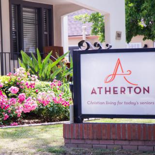 A sign for Atherton residential community surrounded by vibrant flowers and greenery.