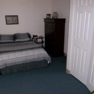 A simple bedroom with a neatly made bed, dresser, and carpeted floor.