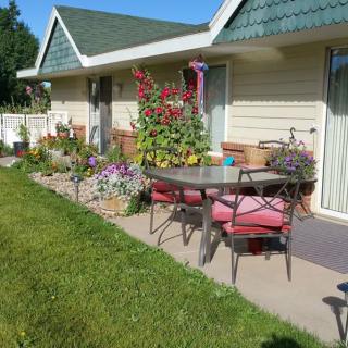 A cozy patio with garden furniture, surrounded by colorful flowers and green lawn.