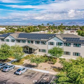 Aerial view of a building with solar panels on the roof, surrounded by trees and a parking lot under a cloudy sky.