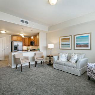 A modern living room with an open kitchen, featuring a sofa, bar stools, and artwork on the walls.