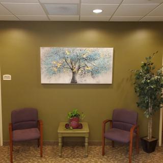 A cozy waiting room with two chairs, a table, and tree artwork on the wall.