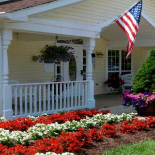 A charming house with a welcoming porch, adorned by an American flag and surrounded by vibrant flower beds.