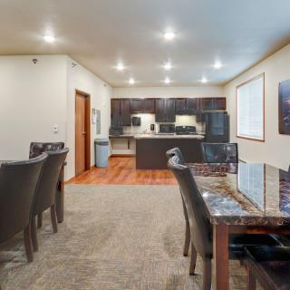 A modern open-plan kitchen and dining area featuring a wooden floor, dark cabinetry, and a dining table with chairs under soft ceiling lighting.