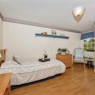A cozy bedroom with a single bed, wooden furniture, and a small desk near the window.