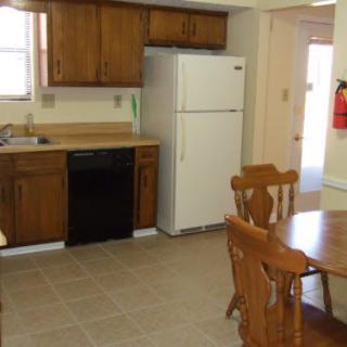 A kitchen and dining area with wooden cabinets, a refrigerator, dishwasher, and a dining table with chairs.