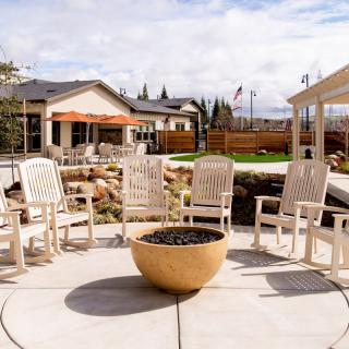 A cozy outdoor patio with arranged chairs around a fire pit, set in a landscaped garden.