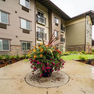 A view of an apartment building exterior with a landscaped courtyard featuring a large flowerpot in the center.