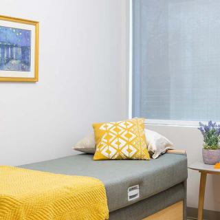 A minimalist bedroom with a single bed, featuring yellow accents and a framed picture on the wall.