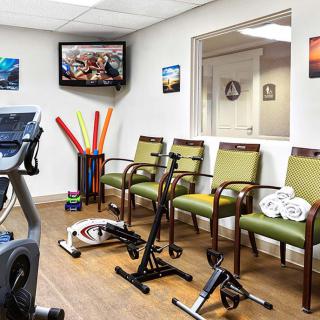 A waiting room with exercise equipment, chairs, and a wall-mounted television.