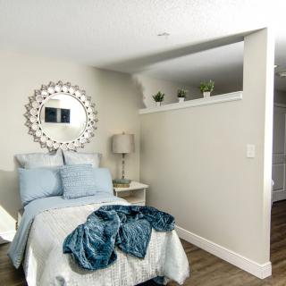A cozy bedroom featuring a bed with blue bedding, a decorative mirror on the wall, and a modern lamp on the nightstand.