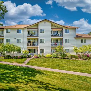 A view of a residential apartment building surrounded by greenery and a well-maintained lawn under a clear blue sky.