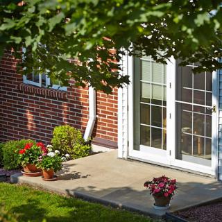A cozy backyard patio with sliding doors, surrounded by potted plants and greenery on a sunny day.