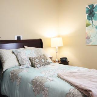 A cozy bedroom with a neatly made bed, featuring decorative pillows and a bedside lamp.