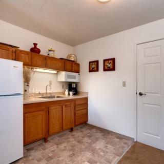 A cozy apartment kitchen with wooden cabinets, a fridge, microwave, and countertop space.