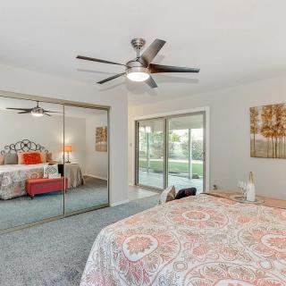 A spacious bedroom with a ceiling fan, mirrored closet doors, and large sliding glass doors opening to a garden view.