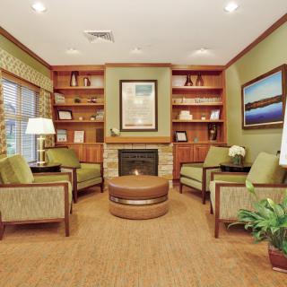 A cozy living room with comfortable seating around a fireplace, surrounded by bookshelves and decorated with plants and artwork.