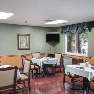 A cozy dining area with set tables and chairs, featuring a wall-mounted television and a window with drapes.