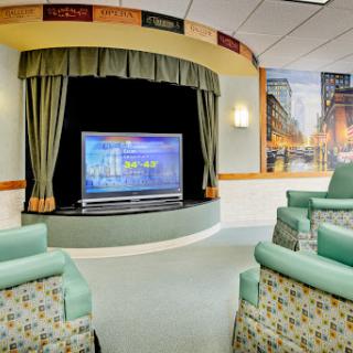 A cozy lounge area in a hospital featuring comfortable seating and a large television for entertainment.