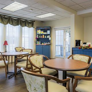 A cozy dining room with tables and chairs, featuring a window with curtains and a cabinet in the corner.