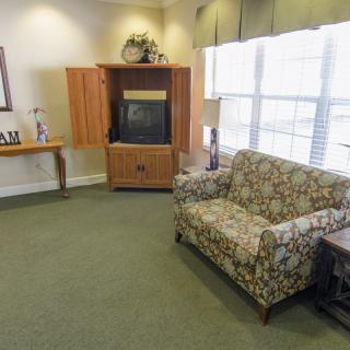 A cozy living room with a floral sofa, TV cabinet, and large windows.