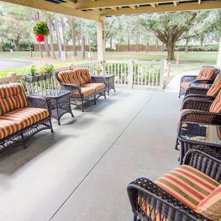 A cozy outdoor patio with wicker furniture and striped cushions under a covered deck, surrounded by trees.