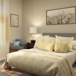 A cozy bedroom with neutral tones, featuring a neatly made bed, decorative pillows, a bedside lamp, and framed artwork on the wall.