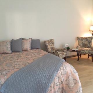 A cozy bedroom with a neatly made bed, floral chairs, and warm lighting.
