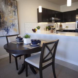 A modern dining area with a dark wooden table and chairs, adjacent to a contemporary kitchen. The space is decorated with a large abstract painting and stylish place settings.