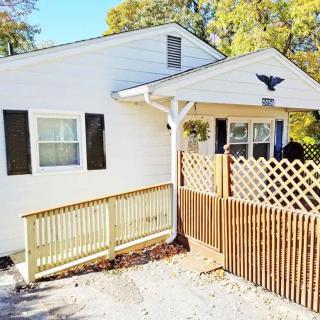 A small white house with a wooden fence and ramp in the front, surrounded by trees.