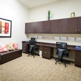 A tidy office workspace with two desks, chairs, and computers, featuring overhead cabinets and decorative items.