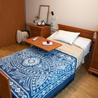 A cozy bedroom featuring a single bed with a blue patterned blanket, wooden furniture, and an alarm clock on the bedside table.