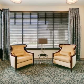 A cozy living room setup featuring two armchairs, a small table with a lamp, and large windows with elegant curtains.