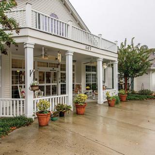 A charming white house with a porch and potted plants on a rainy day.