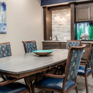A modern dining room with a large table, upholstered chairs, and an integrated aquarium.