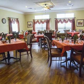 A well-decorated dining room with multiple tables and chairs, featuring red tablecloths and elegant curtains.