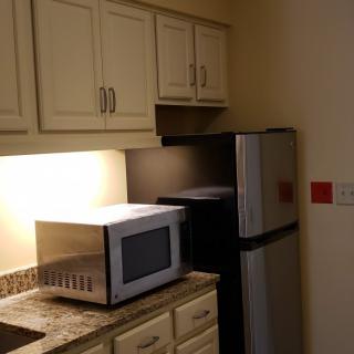 A small kitchen area with a microwave, refrigerator, and cabinets.