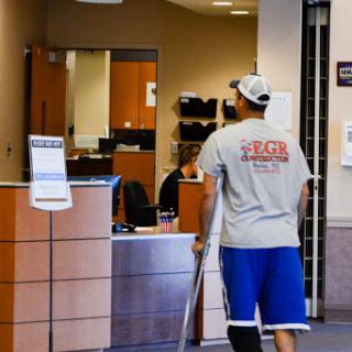 A person using crutches walks through a waiting area in a healthcare facility.