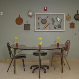 A quaint kitchen dining area with a table and mismatched chairs, adorned with wall decorations featuring vintage cooking utensils.