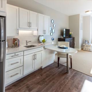 A modern kitchen with white cabinets, wood flooring, and a small dining area.