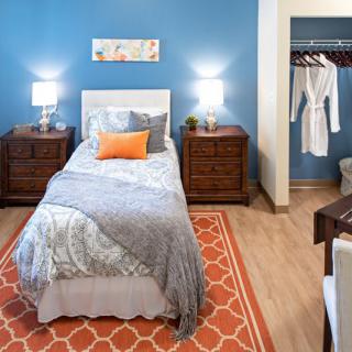 A modern bedroom with a single bed, blue walls, and orange accents.