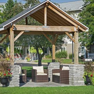 A wooden gazebo with stone pillars and outdoor seating in a garden setting.