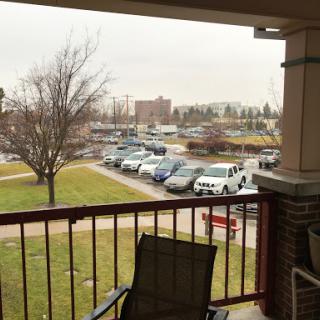 A cloudy day view from a balcony overlooking a parking lot and nearby trees.