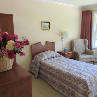 A cozy bedroom with a single bed, an armchair, and a vase of flowers.