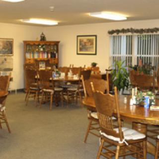Cozy dining room with wooden tables and chairs, decorated with plants and artwork.