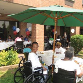 A joyful outdoor gathering for seniors, featuring tables set up with food and decorations, under the shade of umbrellas.