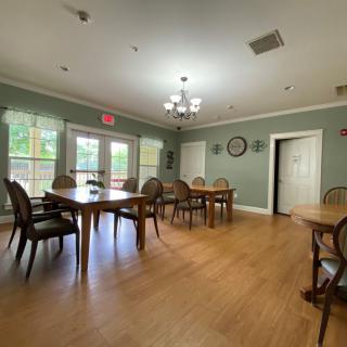 A spacious dining room with wooden floors and multiple tables and chairs, illuminated by a chandelier.