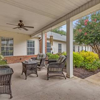 A cozy patio with wicker furniture and a ceiling fan, surrounded by a garden.