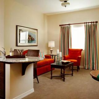 A cozy living room with a red sofa, chairs, and a coffee table, complemented by warm lighting and colorful curtains.